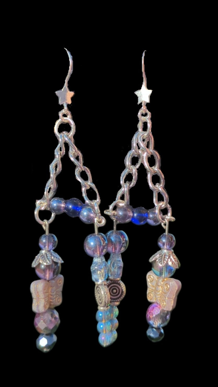 Starry Spell brand earrings held by a hand with a blurred natural background